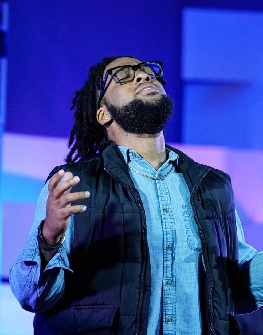 A worshipper with open hands beneath blue stage lighting