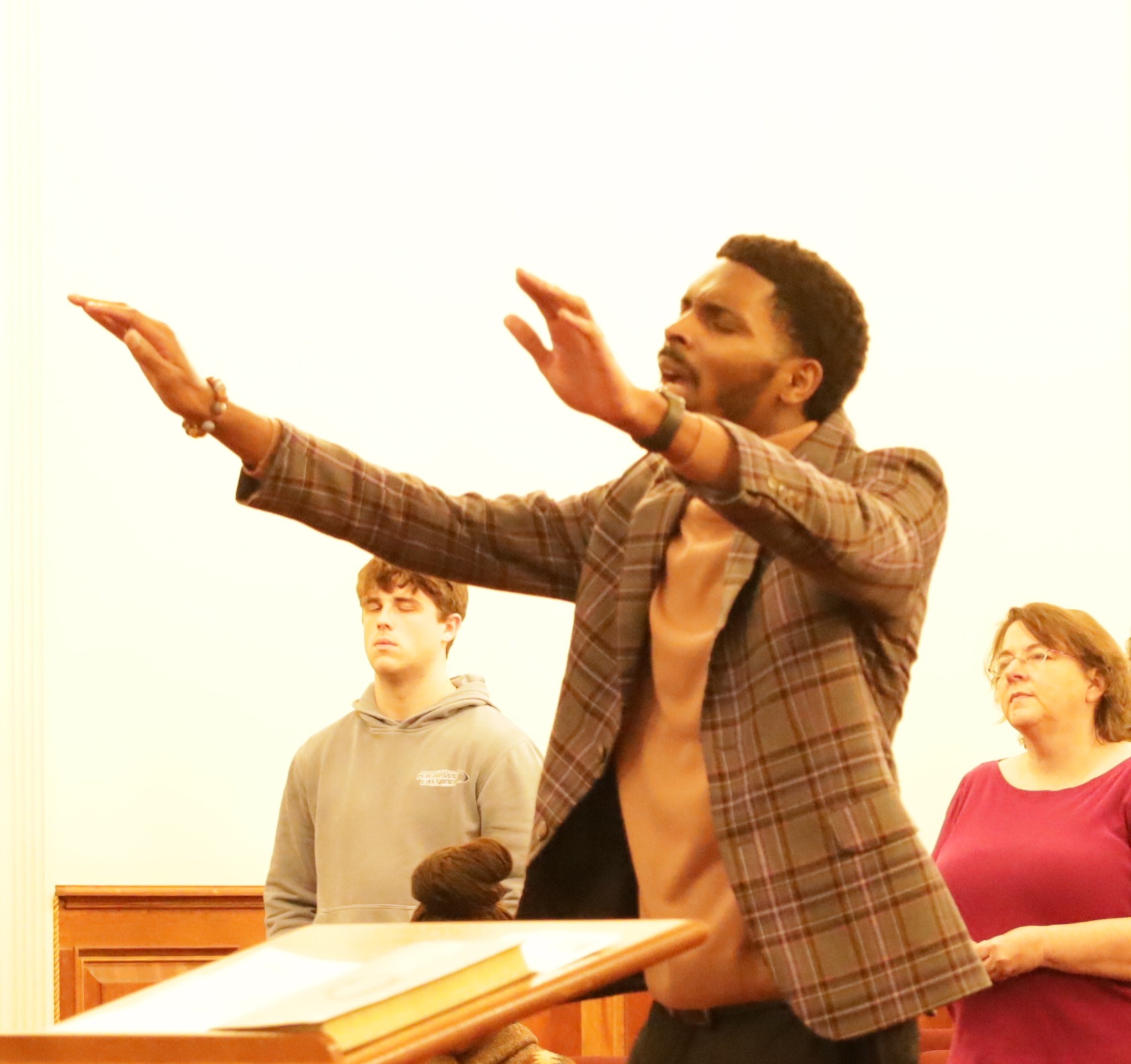 A man at the front of the congregation with both hands raised